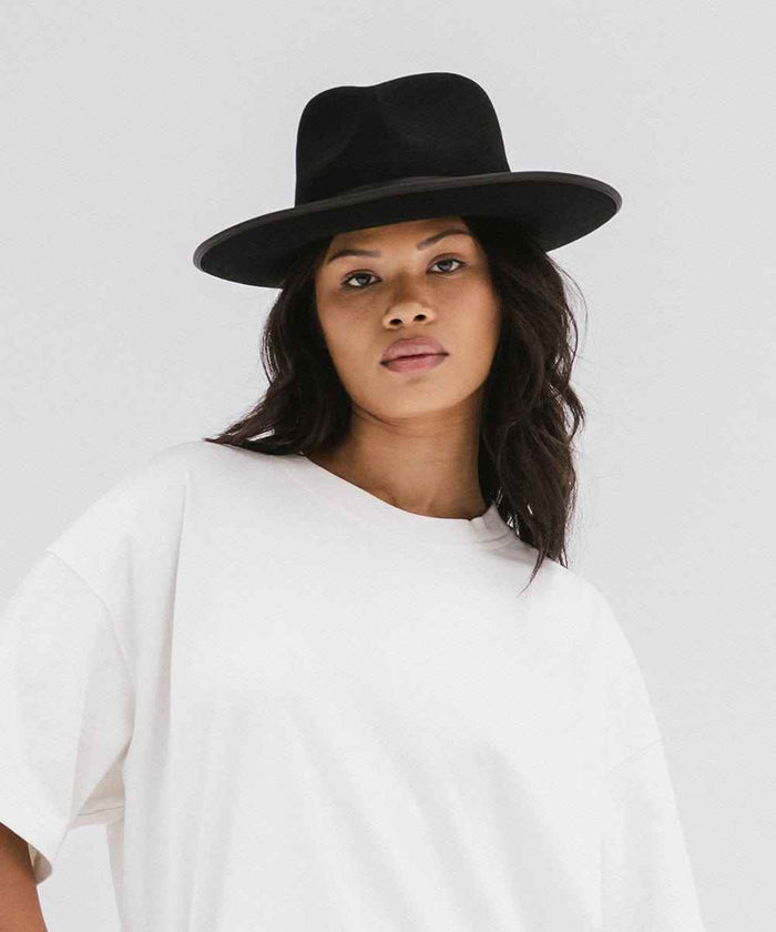 Woman wearing a black fedora hat and a white t-shirt against a plain background #color_black