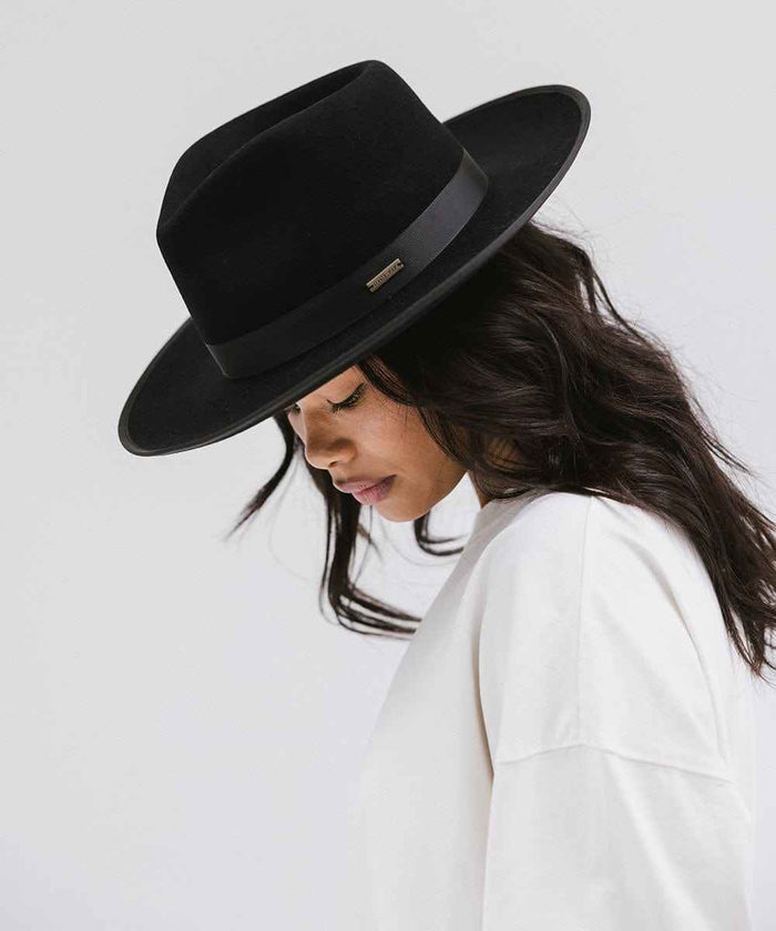 Woman wearing a black fedora hat with a band and a white t-shirt, looking down against a plain background #color_black