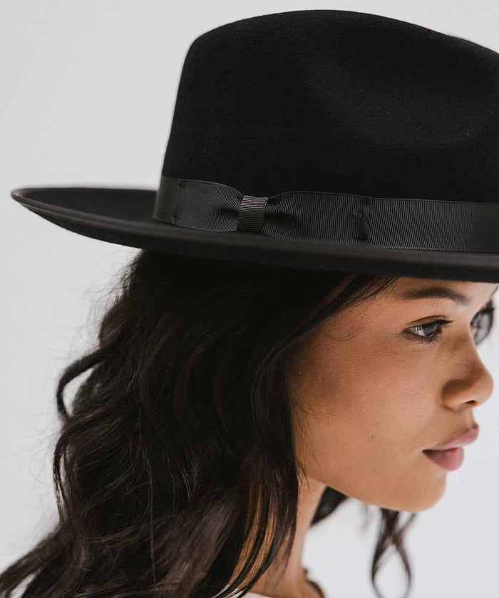 Woman wearing a black fedora hat with a band facing sideways against a plain background #color_black