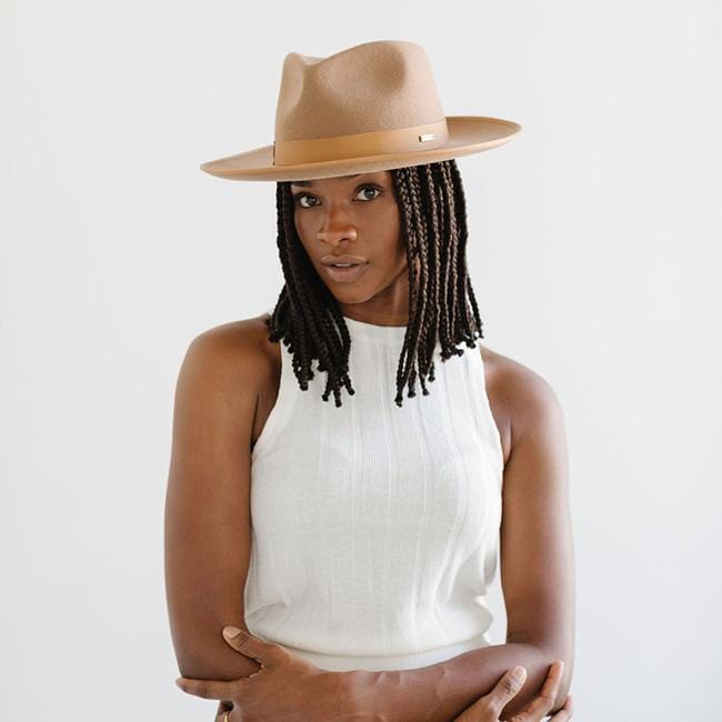 Woman wearing a brown fedora hat with a hat band and a white sleeveless top against a plain background #color_brown