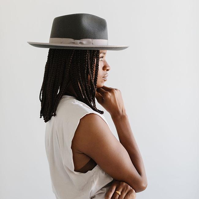 Woman wearing a dark grey fedora hat with a band and a white top, facing sideways against a plain background #color_dark grey