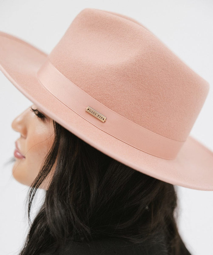 Woman wearing a dusty pink colored fedora hat with a band looking sideways a plain background #color_dusty pink