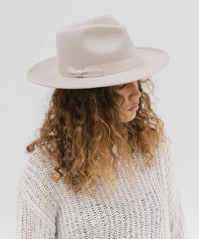 Woman wearing an ivory colored fedora hat with a band and a white knit sweater, looking sideways against a plain background #color_ivory