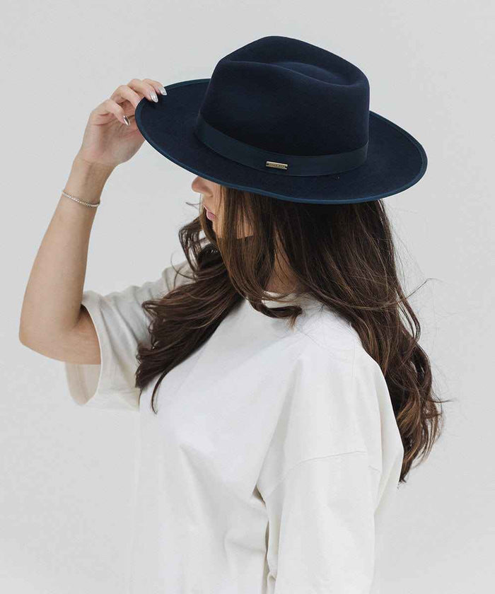 Woman wearing a navy fedora hat with a band and a white t-shirt, facing sideways against a plain background #color_navy