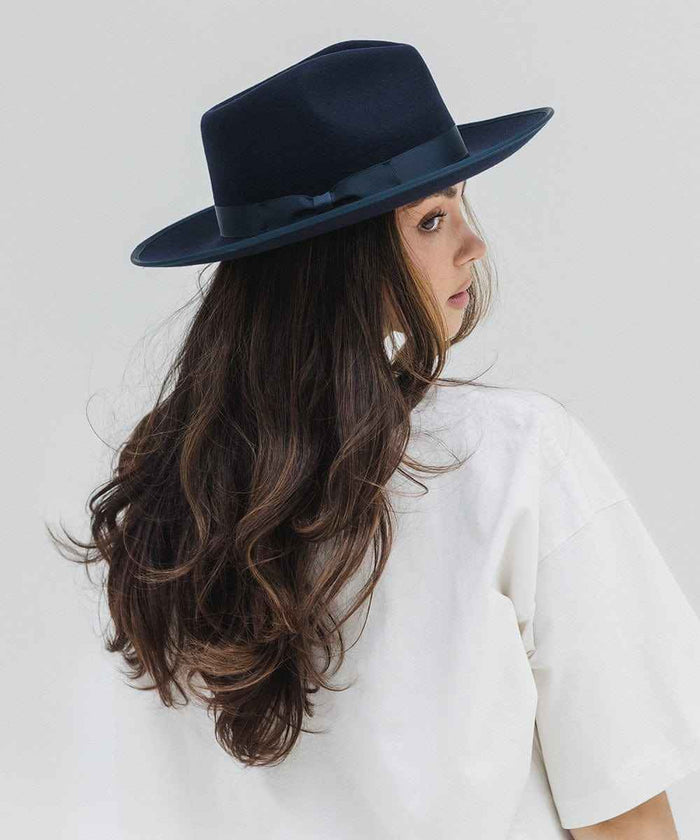 Woman wearing a navy fedora hat with a band and a white t-shirt, looking sideways against a plain background #color_navy