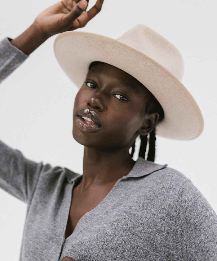 Woman wearing an oatmeal colored fedora hat with a band and a grey shirt against a plain background #color_oatmeal
