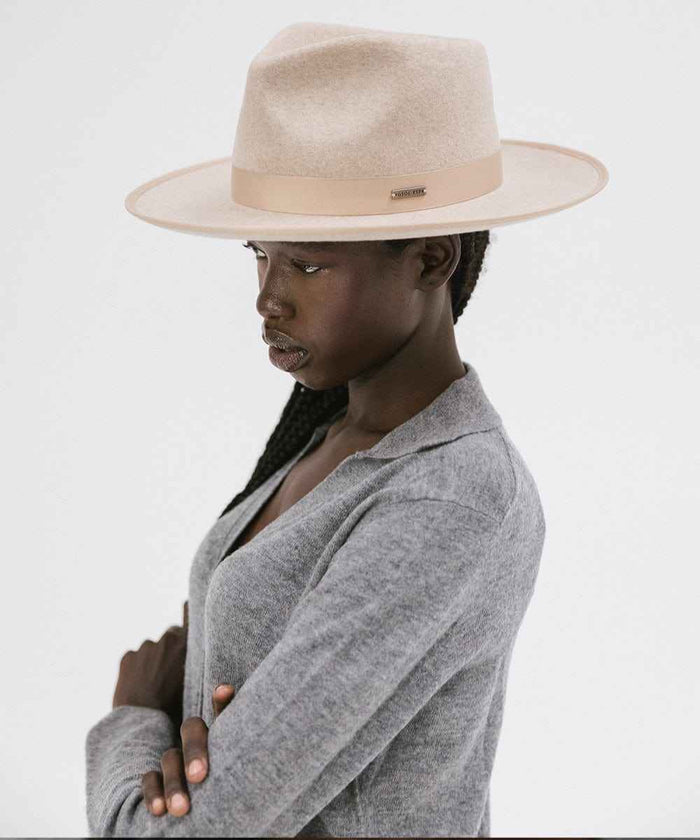 Woman wearing an oatmeal colored fedora hat with a band and a grey shirt, facing sideways against a plain background #color_oatmeal