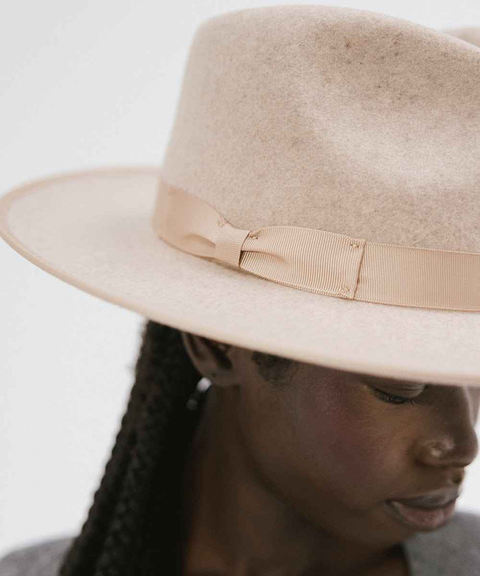 Close up image of a woman wearing an oatmeal colored fedora hat with a band against a plain background #color_oatmeal