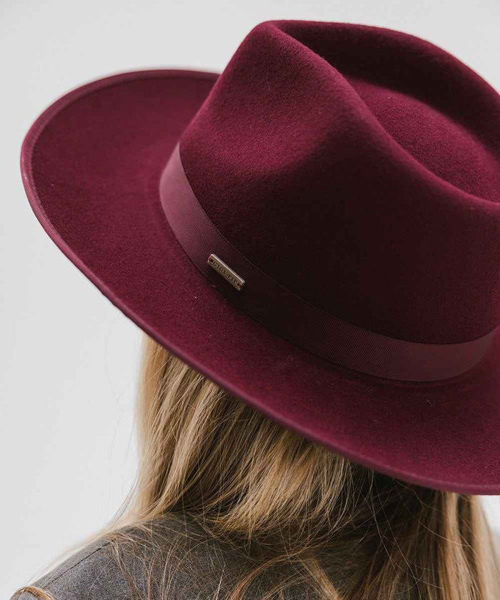 Woman wearing a wine colored fedora hat with a band facing behind against a plain background #color_wine