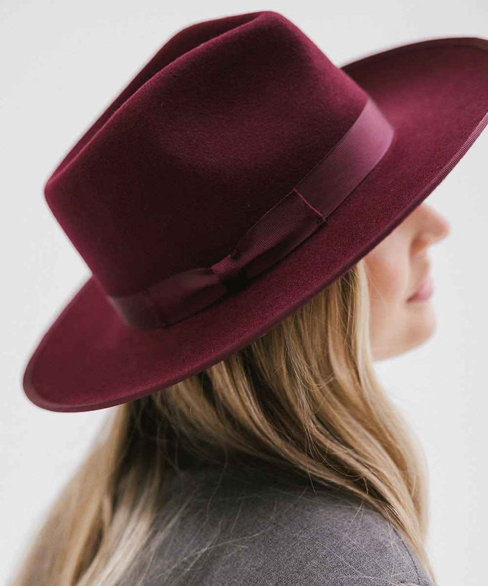 Woman wearing a wine colored fedora hat with a band facing sideways against a plain background #color_wine