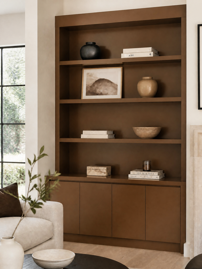 A large built-in wooden bookcase in a warm medium brown finish, styled with books, ceramic vases, a framed print, and bowls in a modern living room setting.