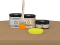 Retique It® Pecan Multipurpose Kit contents with Light Wood Liquid Wood primer, Pecan gel stain alternative, PolyTique It® matte exterior top coat, paintbrush, and yellow sponge displayed on a wood surface.