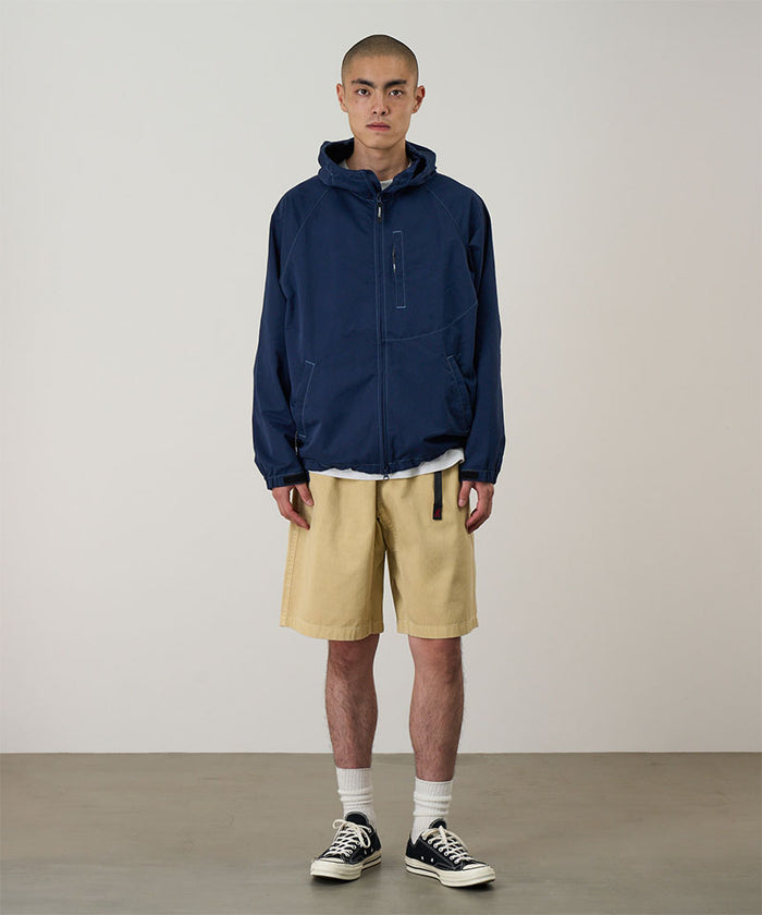 Model wearing a Gramicci Natural Dyed Jam Short in the color chino and a blue hoodie on a light-tone background.