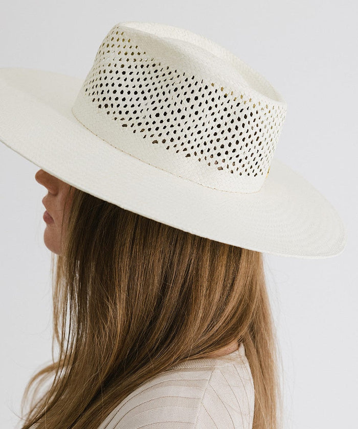 Woman wearing a natural white fedora hat with a wide brim and intricate venting details facing sideways against a plain background #color_natural white