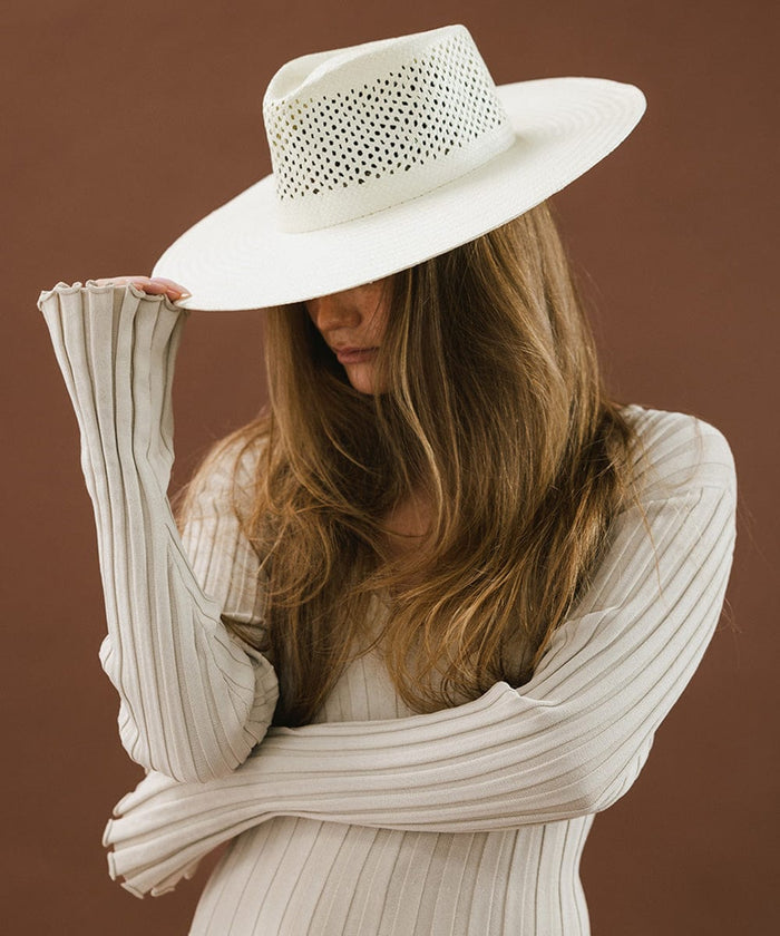 Woman wearing a natural white fedora hat with a wide brim and intricate venting details, and a cream top against a brown background #color_natural white
