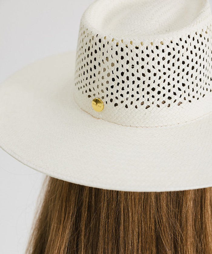 A natural white straw fedora hat with a wide brim, intricate venting details and a gold pin #color_natural white