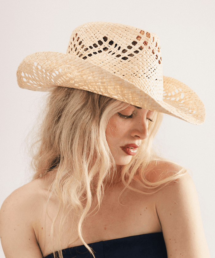 Woman wearing a natural colored straw fedora hat and dark clothing against a plain background #color_natural