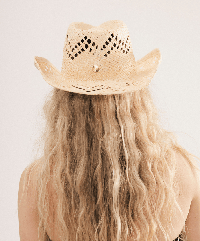 Woman wearing a natural colored straw fedora hat and dark clothing against a plain background #color_natural