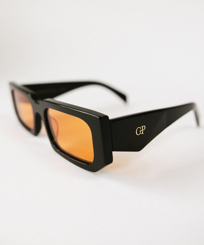 Close up image of sunglasses with black frame and orange lenses on a white background  #color_black
