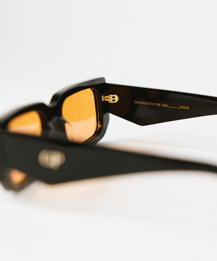 Close up image of sunglasses with black frame and orange lenses on a white background  #color_black