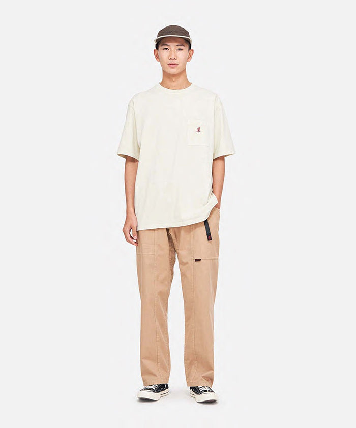 Model wearing a natural pigment Gramicci One Point Tee with a small running man graphic and khaki pants on a light-tone background.