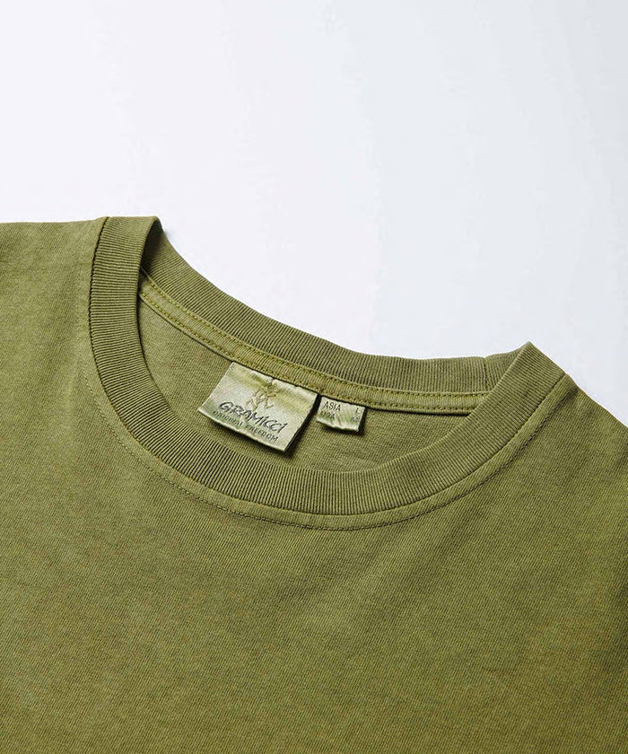 Close-up view of a Gramicci One Point Tee collar in pistachio pigment on a light-tone background.