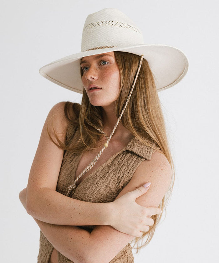 Woman wearing a cream straw hat with a rope hat band and a brown top, posing sideways against a plain background #color_cream
