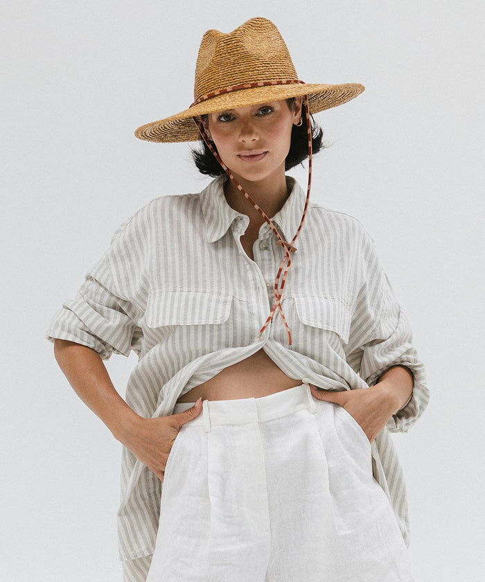Woman wearing a honey colored straw hat, a light colored shirt and white pants against a plain background #color_honey