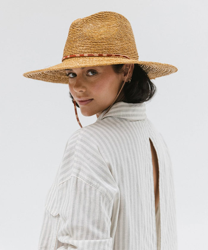 Woman wearing a honey colored straw hat and a light colored shirt against a plain background #color_honey