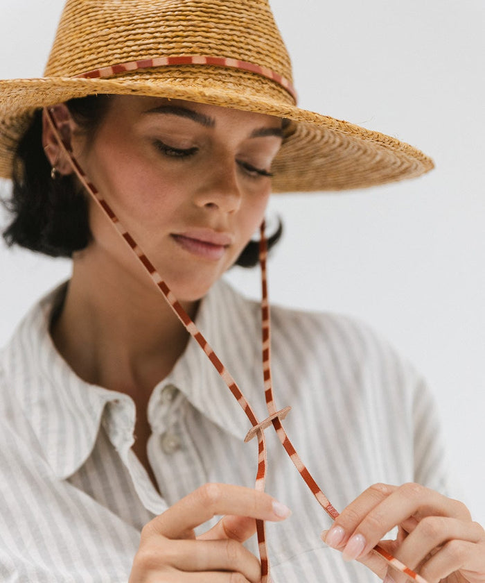 Woman wearing a honey colored straw hat and a light colored shirt, posing against a plain background #color_honey