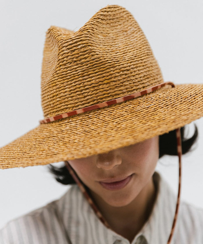Woman wearing a honey colored straw hat against a plain background #color_honey