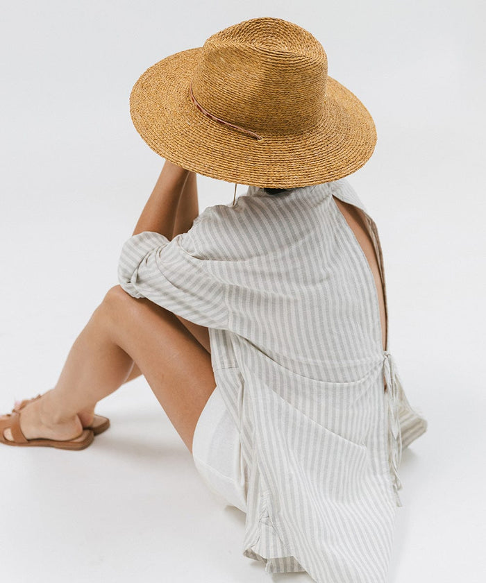 Woman wearing a honey colored straw hat, a light colored shirt, white shorts and brown slippers against a plain background #color_honey