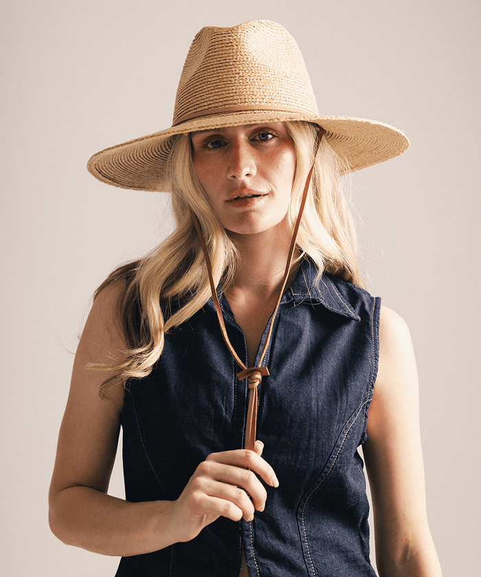 Woman wearing a straw hat and denim vest against a plain background #color_natural