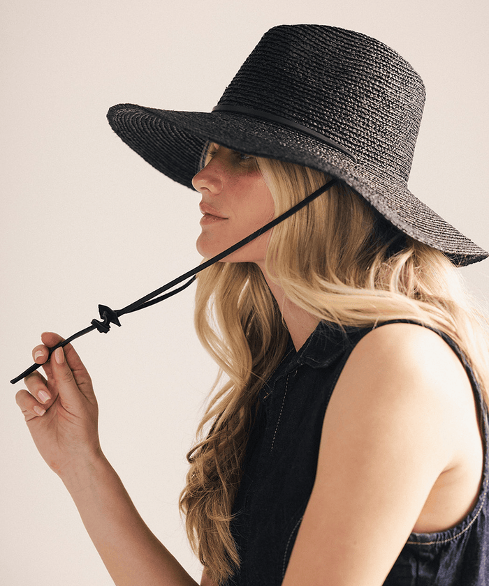 Woman wearing a black straw hat against a plain background #color_black