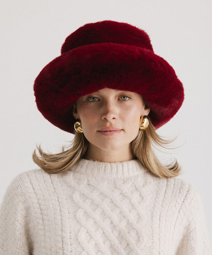 Woman wearing a burgundy faux fur bucket hat and a cream sweater against a plain background #color_burgundy