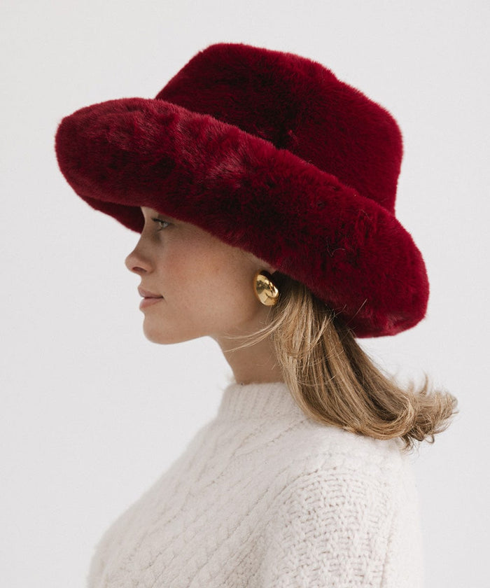 Woman wearing a burgundy faux fur bucket hat and a cream sweater, facing sideways against a plain background #color_burgundy