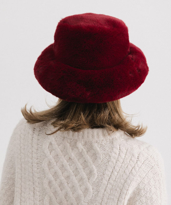 Person wearing a burgundy faux fur bucket hat and a cream sweater against a plain background #color_burgundy