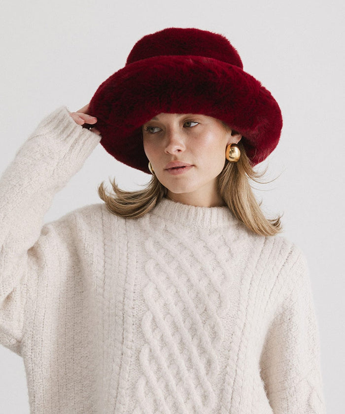 Woman wearing a burgundy faux fur bucket hat and a cream sweater against a plain background #color_burgundy