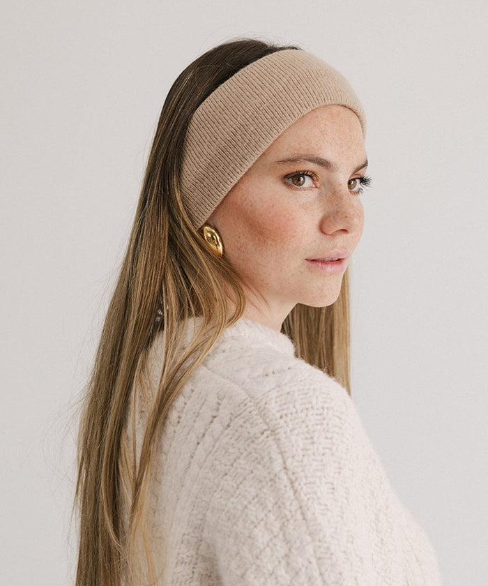 Woman wearing a tan headband and a white sweater, posing sideways against a plain background #color_tan