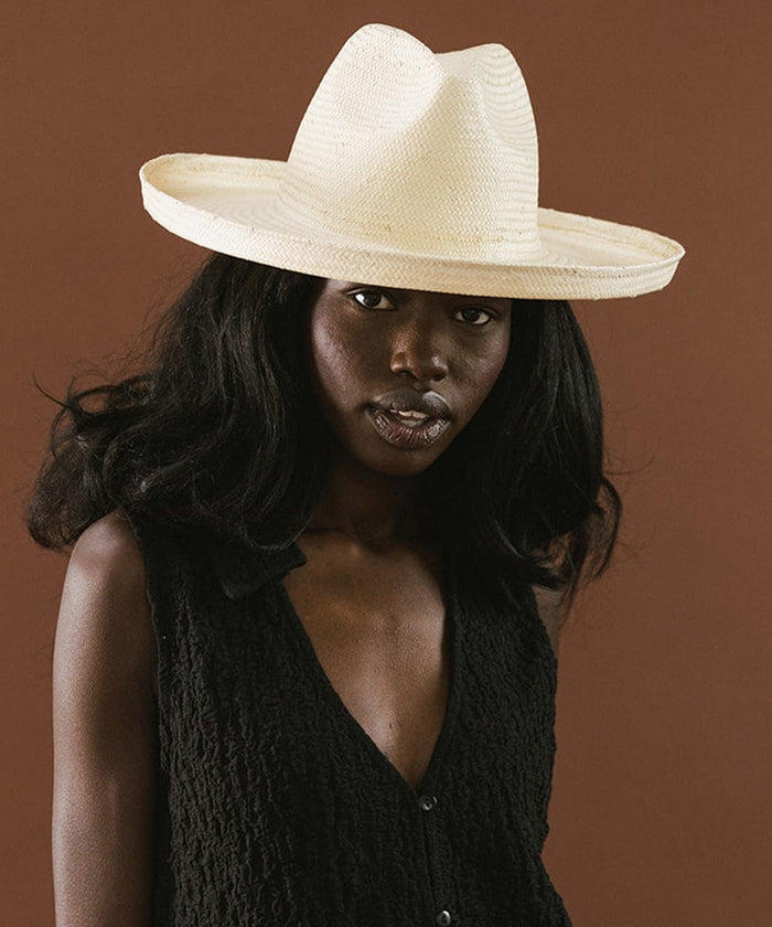 Woman wearing a natural colored pencil brim fedora hat and a black top against a brown background #color_natural