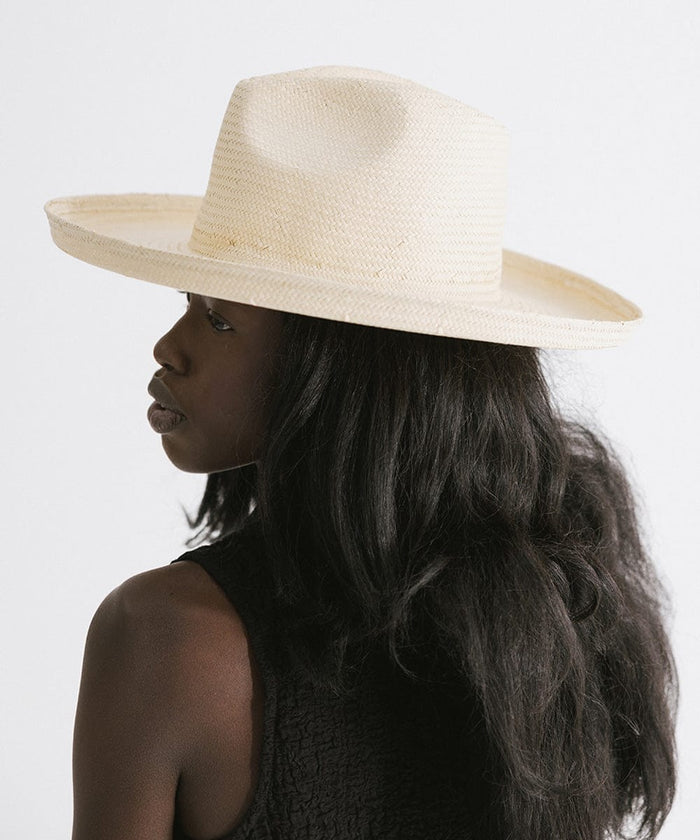 Woman wearing a natural colored pencil brim fedora hat and a black top, looking sideways against a plain background #color_natural
