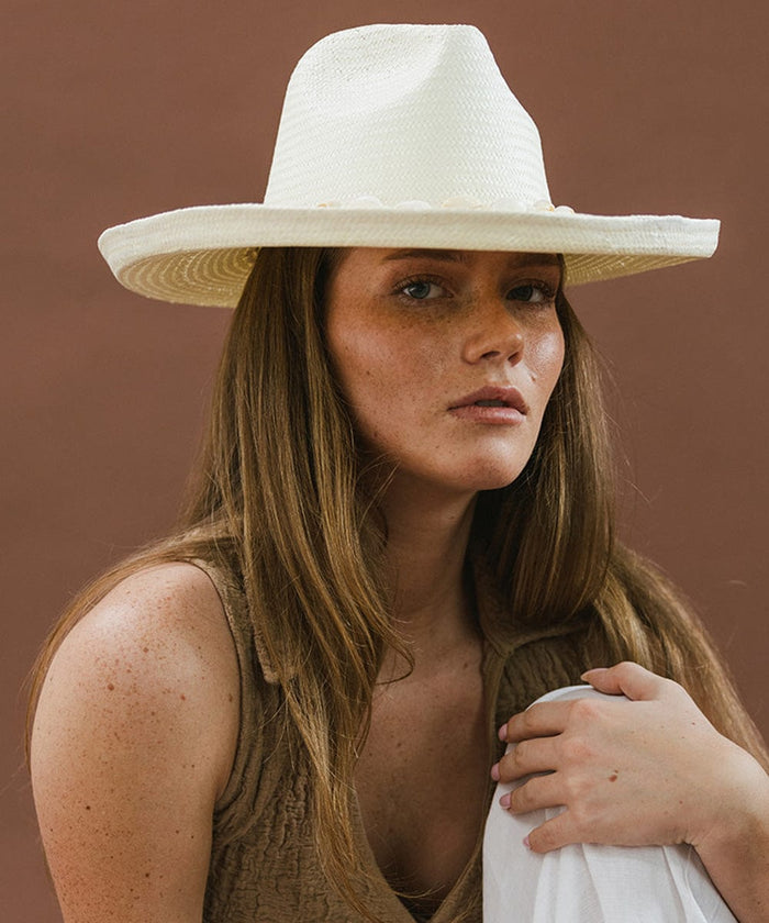 Woman wearing a white pencil brim fedora hat against a brown background  #color_white