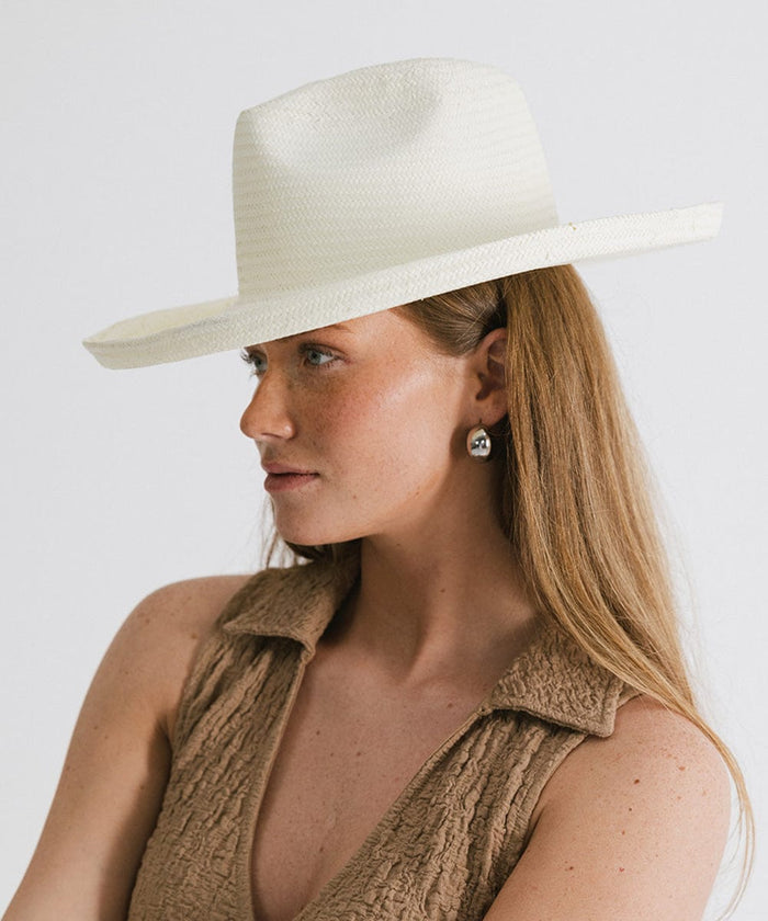 Woman wearing a white pencil brim fedora hat and a brown top, looking sideways against a plain background  #color_white