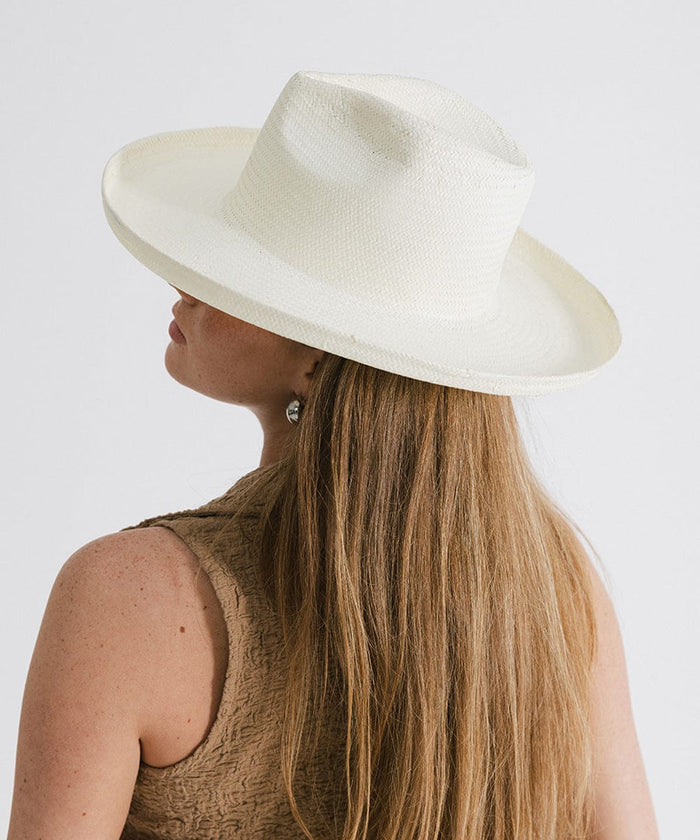 Person wearing a white pencil brim fedora hat and a brown top, facing behind against a plain background  #color_white