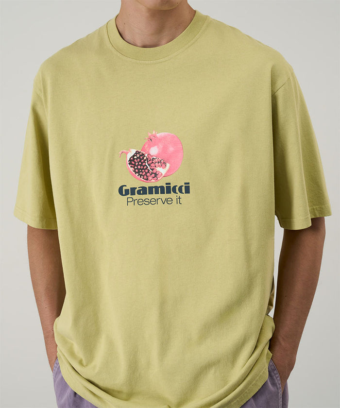 Model wearing a Gramicci lime green Pomegranate Tee with a graphic against a light tone background.