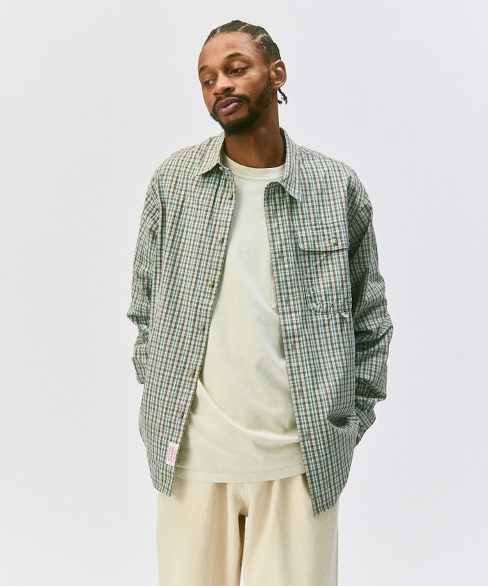 Man wearing a brown plaid Gramicci shirt over a white t-shirt on a light gray background