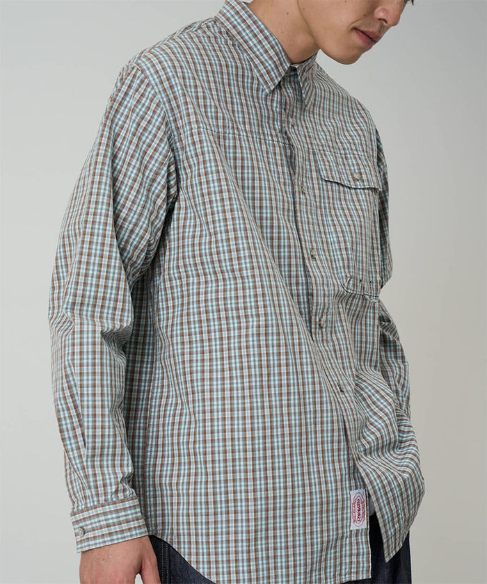 Model wearing a Gramicci brown plaid Poplin Millwood Shirt against a light-tone background.