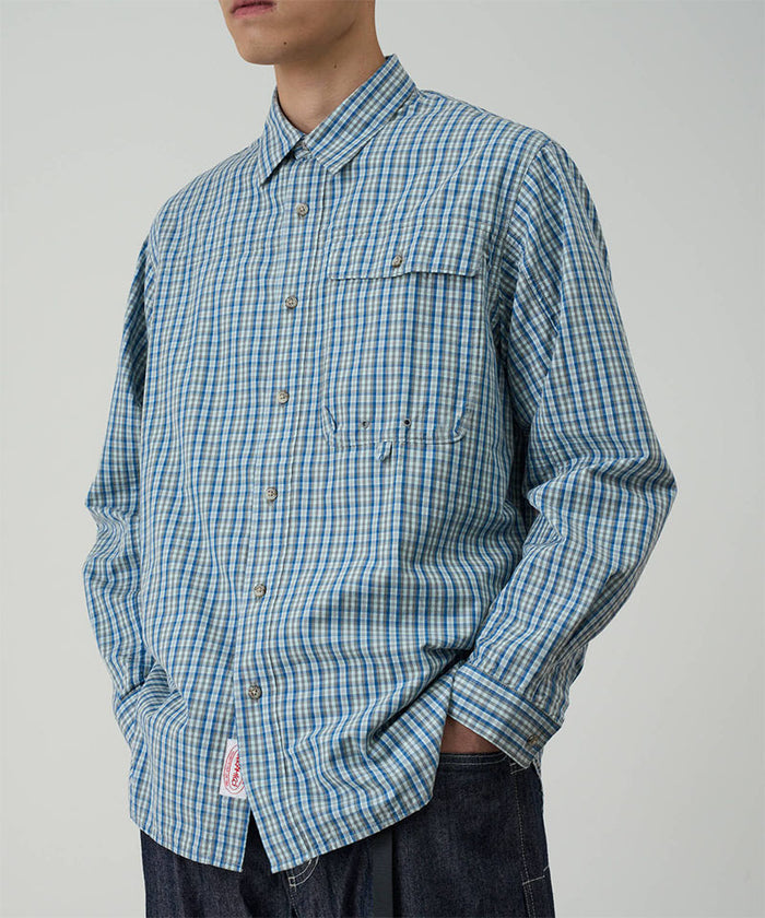 Model wearing a Gramicci blue plaid Poplin Millwood Shirt against a light-tone background.