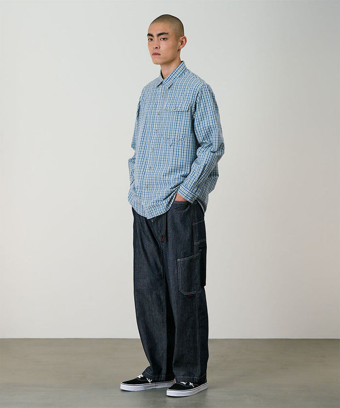 Model wearing a blue plaid Gramicci Poplin Millwood Shirt and blue pants on a light-tone background.