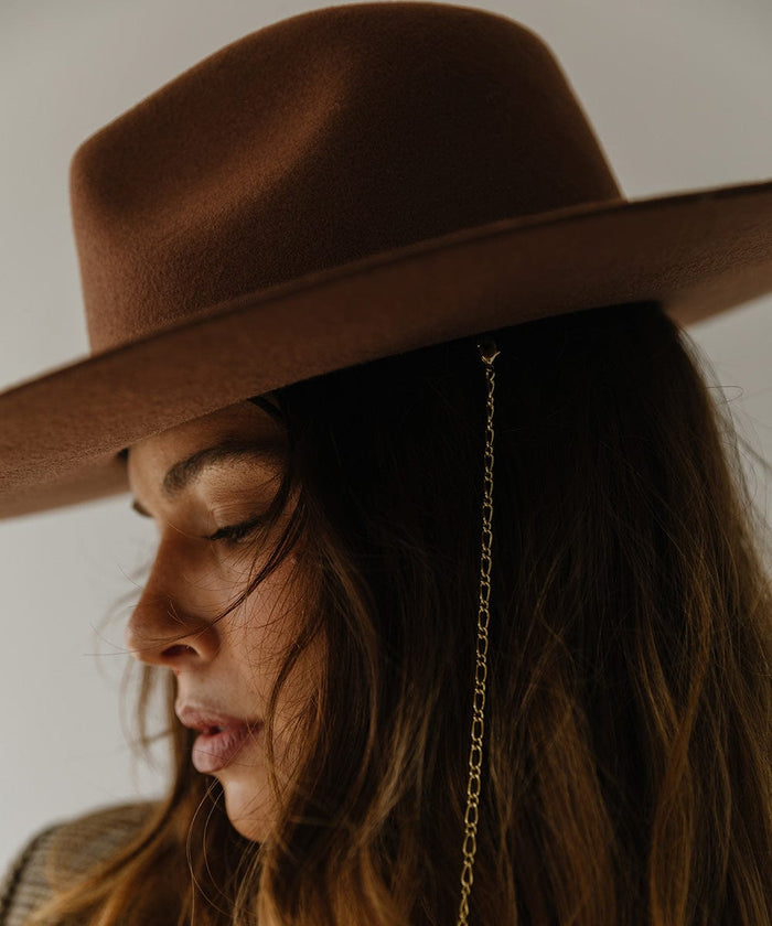 Woman wearing a dark oak colored wide brim fedora hat against a plain background  #color_dark oak